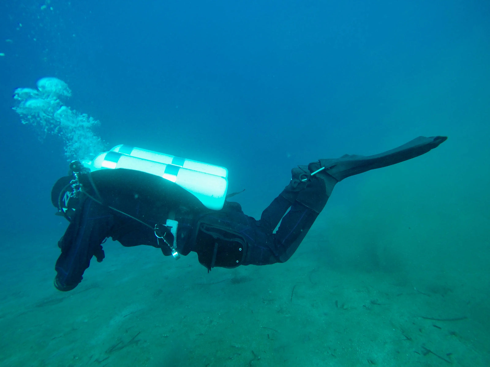 Diver Katerina Pitsou swimming underwater with a rebreather, creating a trail of bubbles, in a blue aquatic environment.