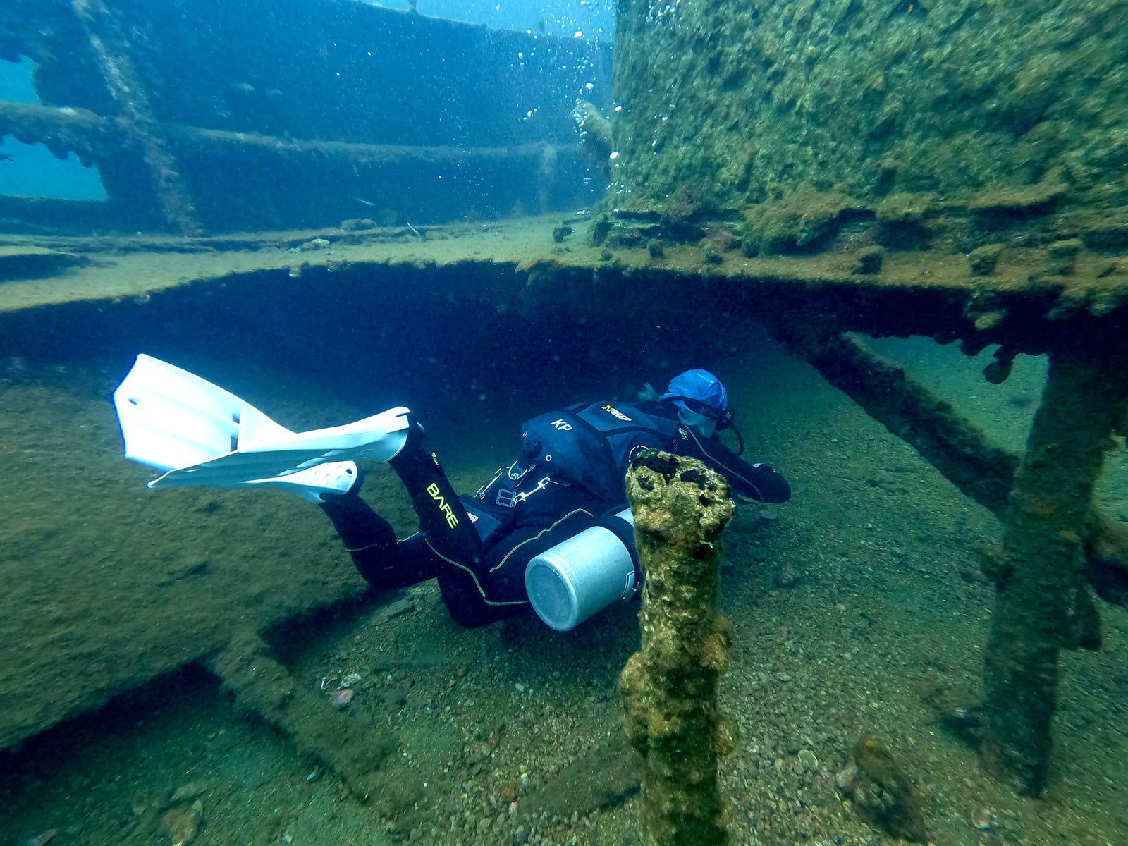 Diver Katerina Pitsou exploring a shipwreck underwater, wearing white fins and a blue helmet, navigating through the rusty structure.