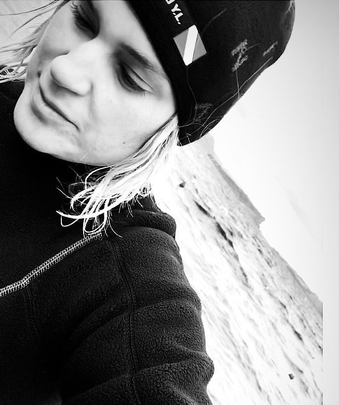 Close-up of Katerina Pitsou wearing a beanie, looking down, with a rocky background in black and white.